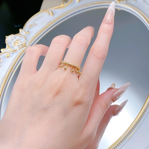 Detail of gold fringe ring with five dangling beads worn by model on hand