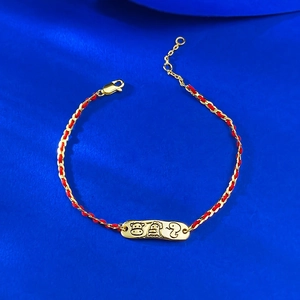 Detail of red rope and gold chain bracelet with engraved cartoon animal metal plate