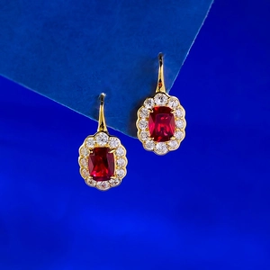 Macro view of gold hook earrings featuring rectangular red rubies and diamond halos