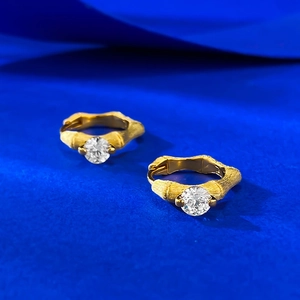 Gold bamboo texture hoop earrings with a large round white zircon on blue background