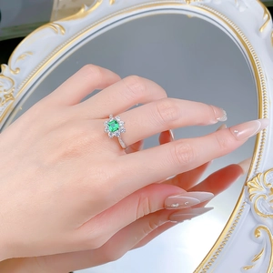 Close-up of a floral S925 silver ring with a rectangular emerald stone and diamond halo
