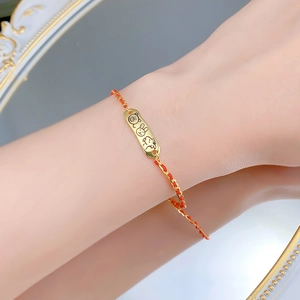 Detail of red braided bracelet with gold charms featuring cartoon animal engravings