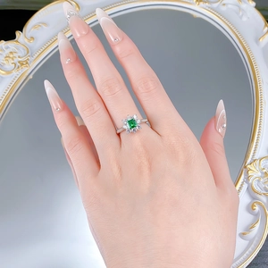 Close-up of flower halo emerald cut green gemstone ring worn on finger near mirror