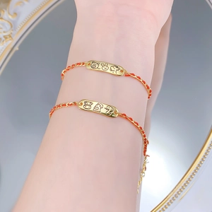 Detail of red woven zodiac bracelet with engraved gold-tone plate and adjustable chain