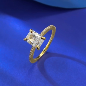 Makroaufnahme Goldring mit Smaragdschliff Stein und Diamanten auf blauem Stoff