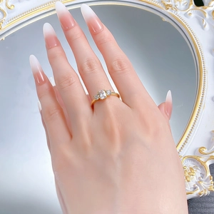 Detail of gold three-stone ring with emerald-cut zirconia on a hand with manicure