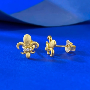 Macro detail of golden fleur-de-lis studs with matte finish and tiny inlaid crystals