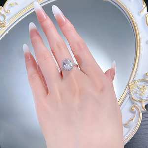 Close-up of 925 silver oval halo ring with sparkling stones on hand with mirror background