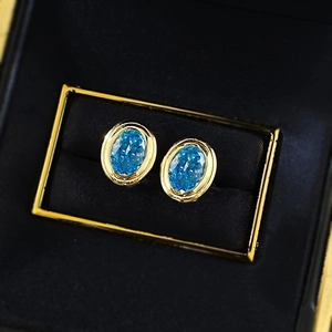 Close-up of gold-plated silver earrings with oval ice-flower cut blue gemstones in a box