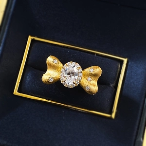 Golden bow ring with oval white stone and pavé accents on blue velvet box