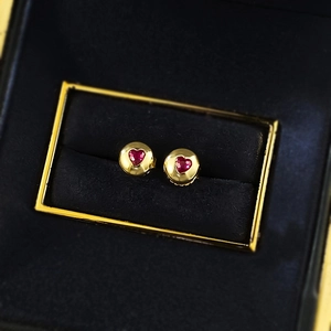 Macro view of gold heart stud earrings with red gemstones in a black velvet jewelry box