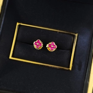 Macro view of gold clover stud earrings with ruby-pink gemstones in a luxury jewelry box
