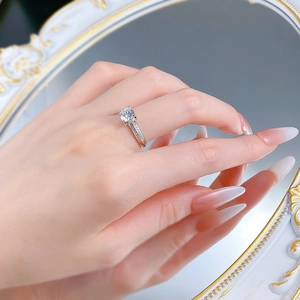 Elegant six-prong solitaire ring with side stones worn on finger against mirror