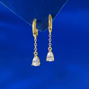 Macro view of teardrop crystal tassel earrings in gold finish on blue display