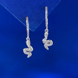 Macro detail of silver snake earrings with pavé crystals and pear-cut stone on blue background