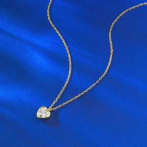Macro shot of heart-shaped crystal pendant on golden chain over blue silk background