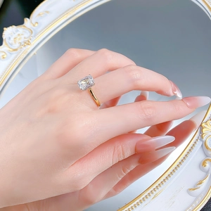 Detail of emerald cut rectangle ring in gold finish worn by model with mirror background