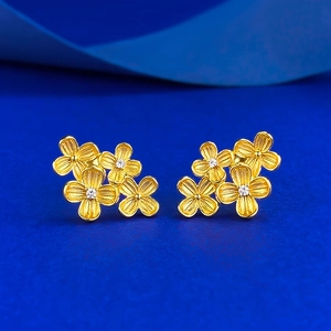 Detail of gold flower studs with brushed texture and small zircon center on blue background