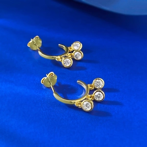 Golden semi-circle earrings with dangling zircon charms on vibrant blue background