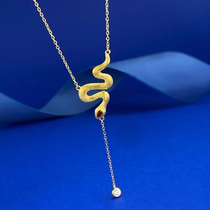 Macro detail of gold snake necklace with brushed texture, red gem and white zircon