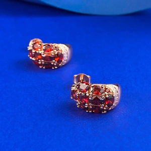 Boucles d'oreilles créoles en or rose avec trois rangées de grenats ovales sur fond bleu