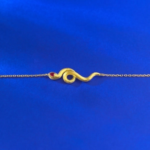 Golden brushed snake bracelet featuring a sparkling pear-cut red gemstone on blue silk