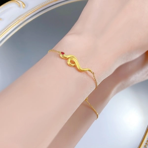 Detail of brushed gold snake bracelet with a red ruby eye on a model's wrist