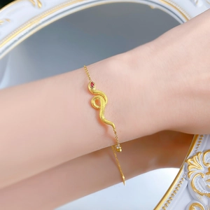 Macro shot of gold snake bracelet with brushed finish and inlaid red gemstone
