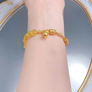 Détail d'un bracelet tressé jaune avec des breloques dorées en forme de gourde et pièces