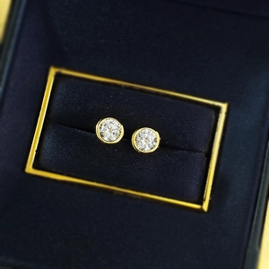 Macro shot of 5mm round cubic zirconia stud earrings in gold bezel setting on velvet