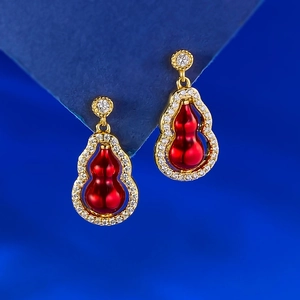Gros plan sur des boucles d'oreilles gourde dorées avec insert rouge et pavé de diamants