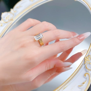 Detail of emerald cut gemstone ring with multi-layer gold band on model's hand