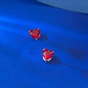 Close-up of heart-cut red ruby stud earrings with S925 silver prong setting on blue background