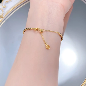 Macro detail of S925 silver coin charm and black beads on a gold-plated bracelet