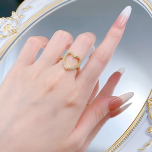 Gros plan d'une bague cœur dorée sertie de pierres portée par un mannequin devant un miroir