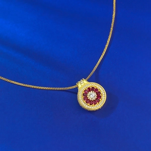 Macro detail of a gold compass pendant with red rubies and a white center stone