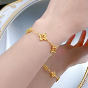 Détail d'un bracelet trèfle doré avec bords perlés et pierres étincelantes sur un poignet