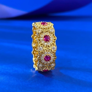 Detailed close-up of retro hollow lace pattern gold ring with red and white gemstones