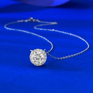Macro shot of 7mm halo round diamond pendant on silver chain against royal blue backdrop