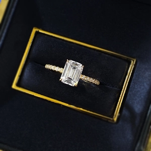 Macro view of emerald cut crystal ring with pavé diamond band in blue velvet box