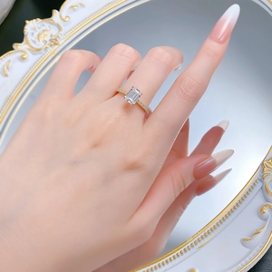 Elegant gold ring with emerald cut white gem and pavé diamonds worn on finger