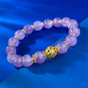 Macro detail of 10mm amethyst bead bracelet with gold filigree charm on blue background