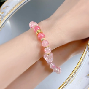 Detail of pink crystal beaded bracelet with golden feather charm worn on woman wrist