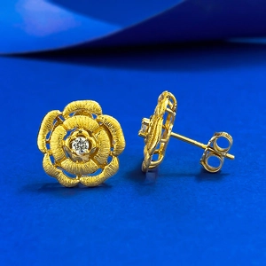 Macro shot of gold-plated camellia flower stud earrings with brushed texture and small zircon