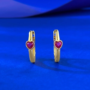 Elegant gold heart earrings with red rubies and beaded bezel on a blue background
