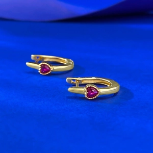 Detail of heart-shaped gold-plated silver earrings with red gemstone in bezel setting