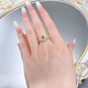 Macro detail of V-shaped gold ring with pear-cut emerald and sparkling white zircons