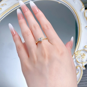 Close-up of a heart-shaped diamond gold ring worn on a finger with white manicure
