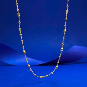 Detail of gold beaded necklace with faceted geometric beads on deep blue background