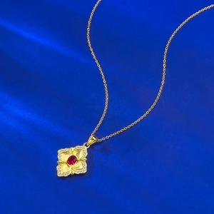 Detailed macro of gold S925 silver necklace with red ruby flower pendant on blue silk